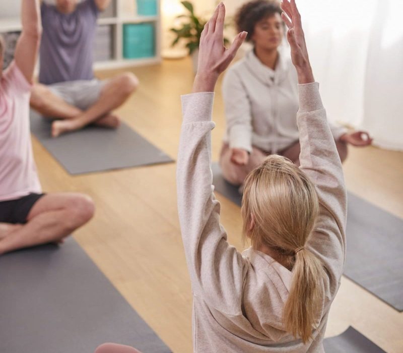 Grupo-con-un-profesor-sentado-en-colchonetas-de-ejercicio-estirandose-en-una-clase-de-yoga